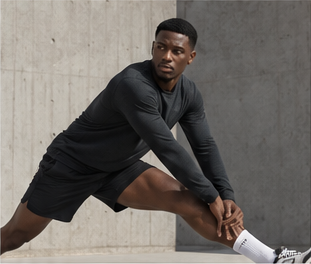 Model in a black training top and shorts stretching against a concrete wall