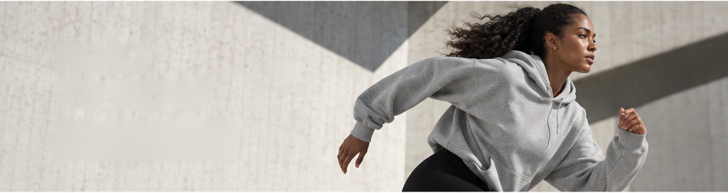 Runner in a heather grey hoodie mid stride against a concrete wall